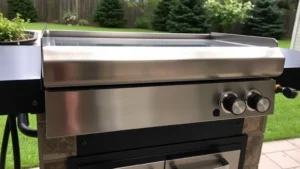 Outdoor Blackstone griddle with natural gas line connection, stainless steel cooking surface with flames visible underneath, residential backyard setting with green lawn and trees in background, professional installation visible