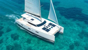 Modern recreational sailboat with solar panels integrated into hull design sailing through crystal clear turquoise water, showing sustainable marine technology in natural sunlight