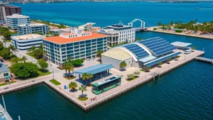 Aerial view of Tampa Bay waterfront with modern electric bus station and solar panels on municipal buildings, blue water visible, green urban development