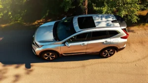 Overhead view of modern silver Honda CR-V hybrid parked in natural setting with trees and sunlight, showing sleek aerodynamic design and eco-conscious styling without any text or labels visible