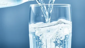 Crystal clear sparkling water being poured into a glass with visible bubbles and carbonation, natural sunlight highlighting the liquid, minimalist background with fresh water droplets